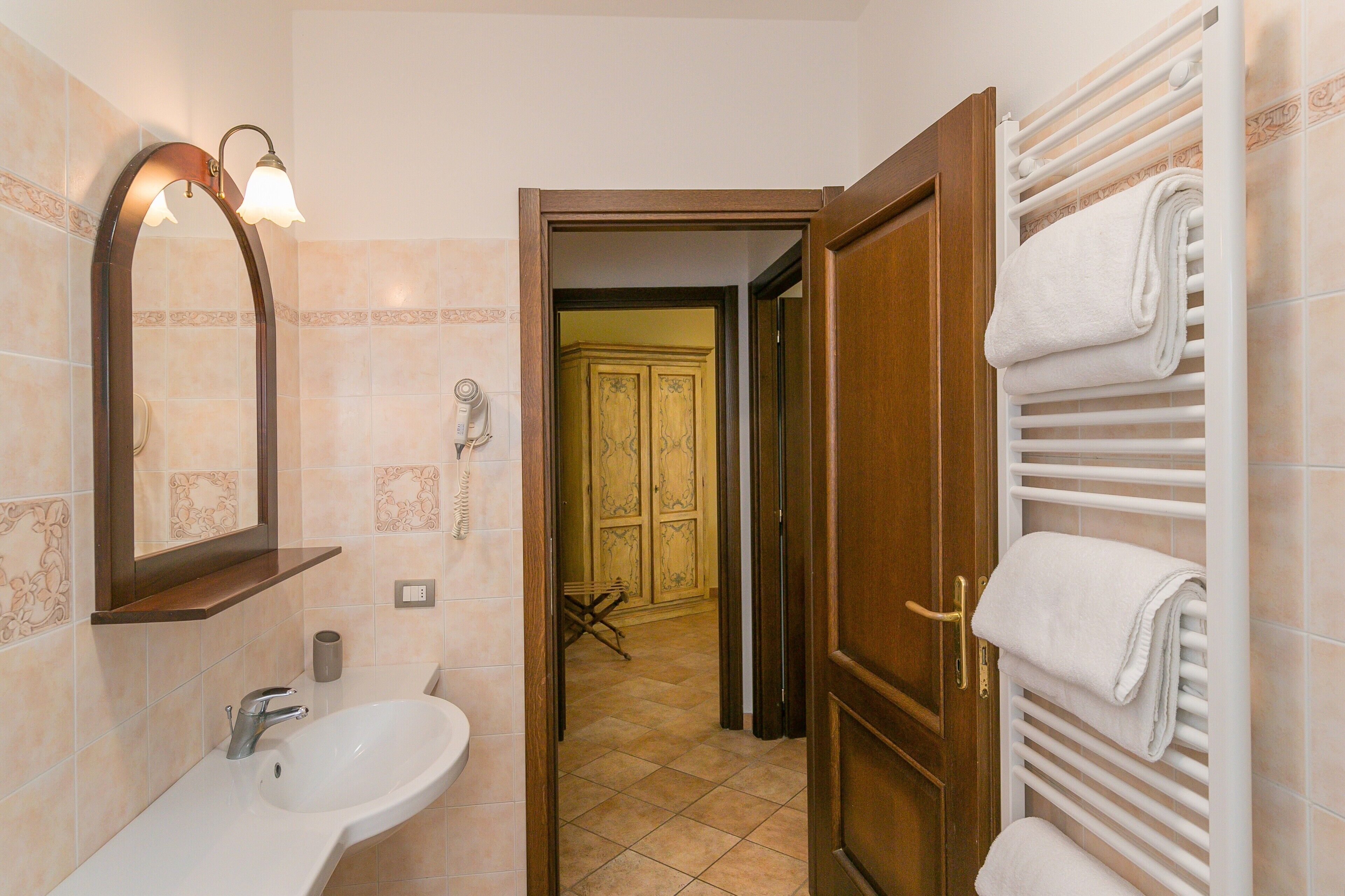 Un baño con lavamanos, espejo, toallero y una puerta que da a otra habitación.