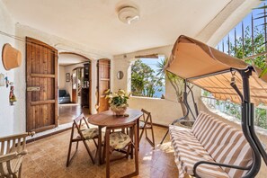 Un patio con tavolo in legno, sedie, un divano a righe e una pergola con tenda.