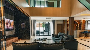 Ein modernes Wohnzimmer mit einem schwarzen Ledersofa, einem Glastisch und einem Flachbildfernseher, der an einer schwarzen Marmorwand angebracht ist.