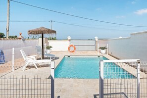 A swimming pool with a white fence, lounge chairs, and a lifebuoy.