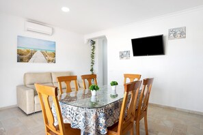 A dining area with a glass table, chairs, a sofa, and a TV.