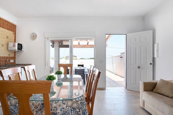 A dining area with a glass-top table, wooden chairs, a potted plant, and a white door leading outside.