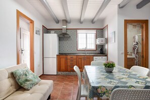 A compact kitchen with wooden cabinets, a white refrigerator, and a dining table with a floral tablecloth. - Vacation Home "Casa Sheila" with Private Pool, 2 Private Terraces & Wi-Fi (Conil)