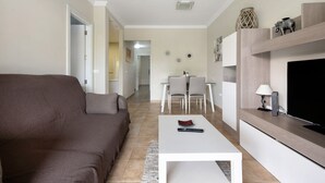 A living room with a sofa, a coffee table, a TV, and a dining area with chairs and a table.