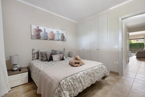 Un dormitorio con cama, mesita de noche, lámpara y un cuadro de jarrones.