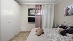 A bedroom with a bed, a TV mounted on the wall, a window with curtains, and a painting on the wall.