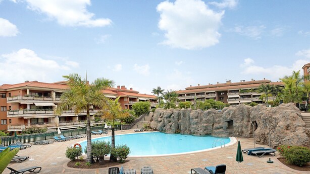 A hotel with a swimming pool, lounge chairs, and a rock formation.