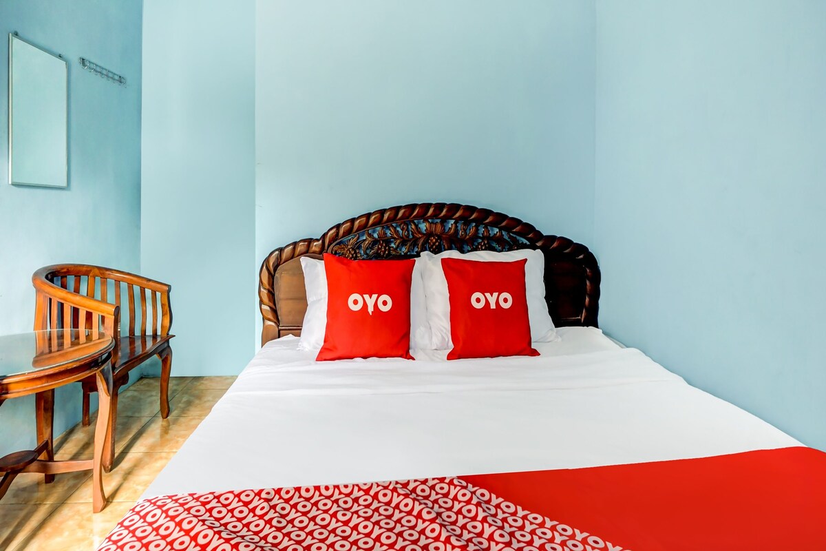 A room with a bed, two red pillows with "OYO" text, a wooden chair, and a patterned headboard.