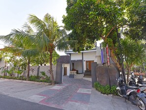 A modern building with a paved entrance, surrounded by palm trees and other greenery. - Hotel O Homestay Antara (Melaya)