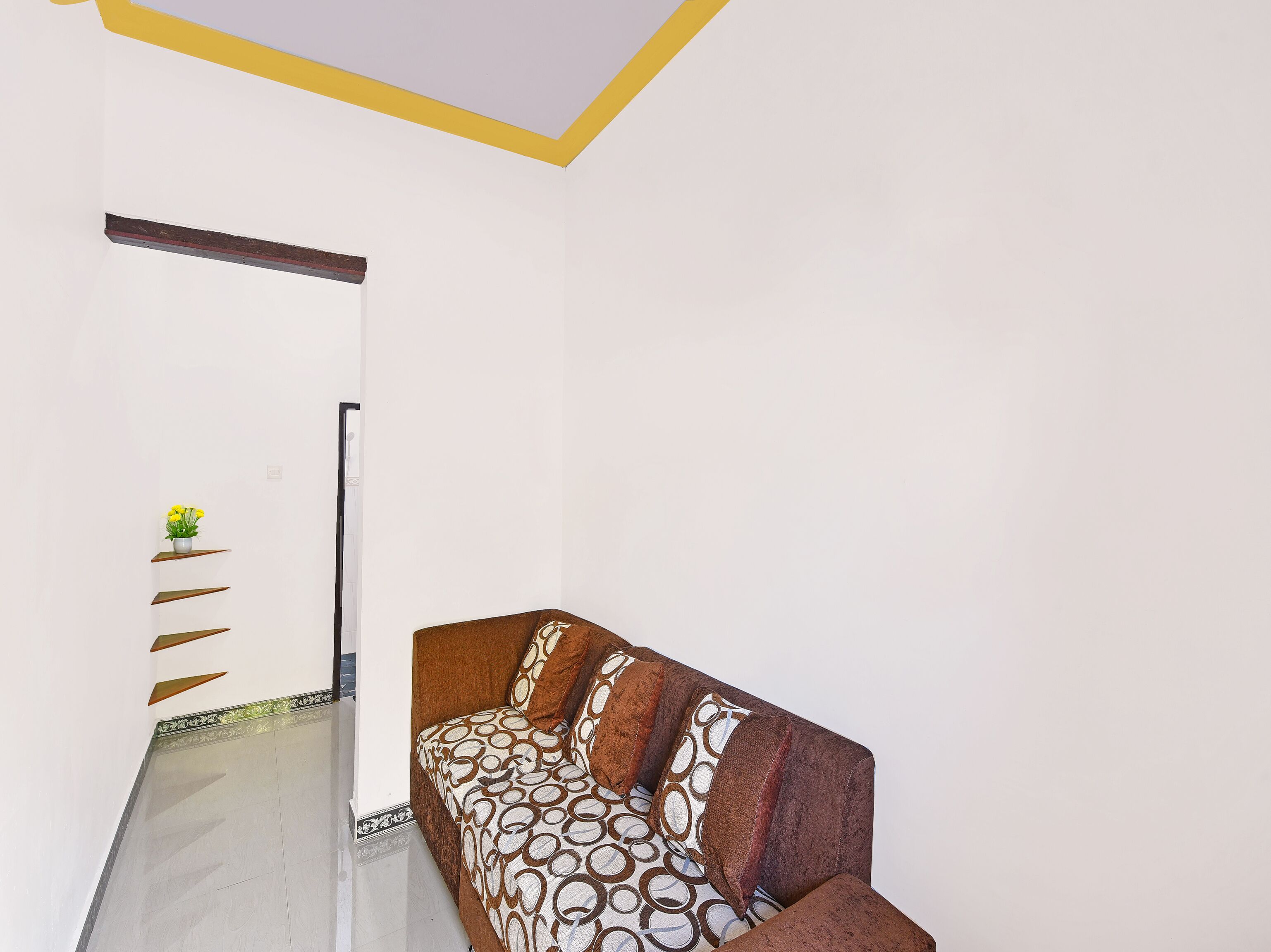 A room with a sofa, a wall-mounted shelf with a plant, and a patterned floor.