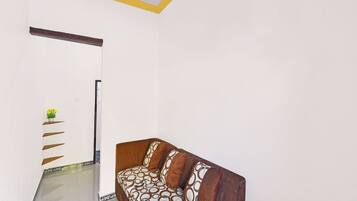 A room with a sofa, a wall-mounted shelf with a plant, and a patterned floor.