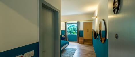 Ein Hotelzimmer mit Bett, kleinem Schreibtisch, einem Fenster mit Vorhängen und einer Tür zu einem anderen Raum.