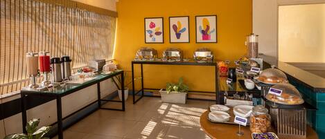 A breakfast buffet area with various food items and a coffee station.