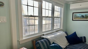 Ein Zimmer mit großem Fenster, einem Bett mit gestreifter Bettwäsche, einer Decke und einer Schachtel mit Yahtzee-Würfeln auf einer Holzkiste.