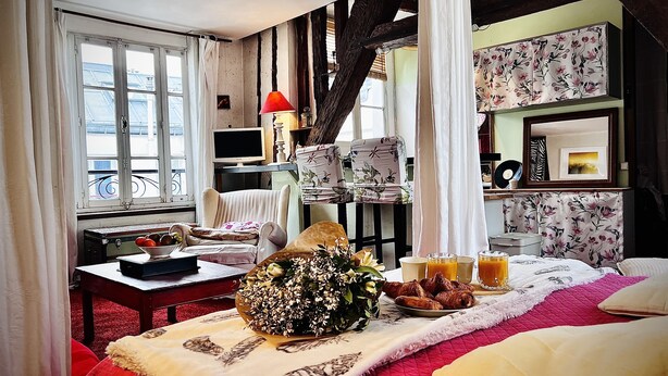 Ein gemütliches Zimmer mit einem Bett, einem Tisch mit Frühstücksangeboten, einem Fernseher und einem Fenster mit Vorhängen.