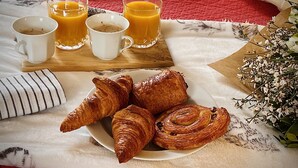 Frühstücksgedecke mit Croissants, Orangensaft und Kaffee auf einem Bett mit einer roten Steudeckdecke.
