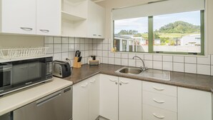 A modern kitchen with white cabinets, a stainless steel sink, a dishwasher, a microwave, and a window with a view of a residential area.