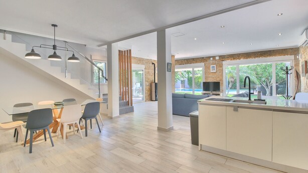 A modern kitchen with a central island, a dining area with a table and chairs, and a staircase leading to an upper level. - Modern villa in Las Rotas with air conditioning (Denia)