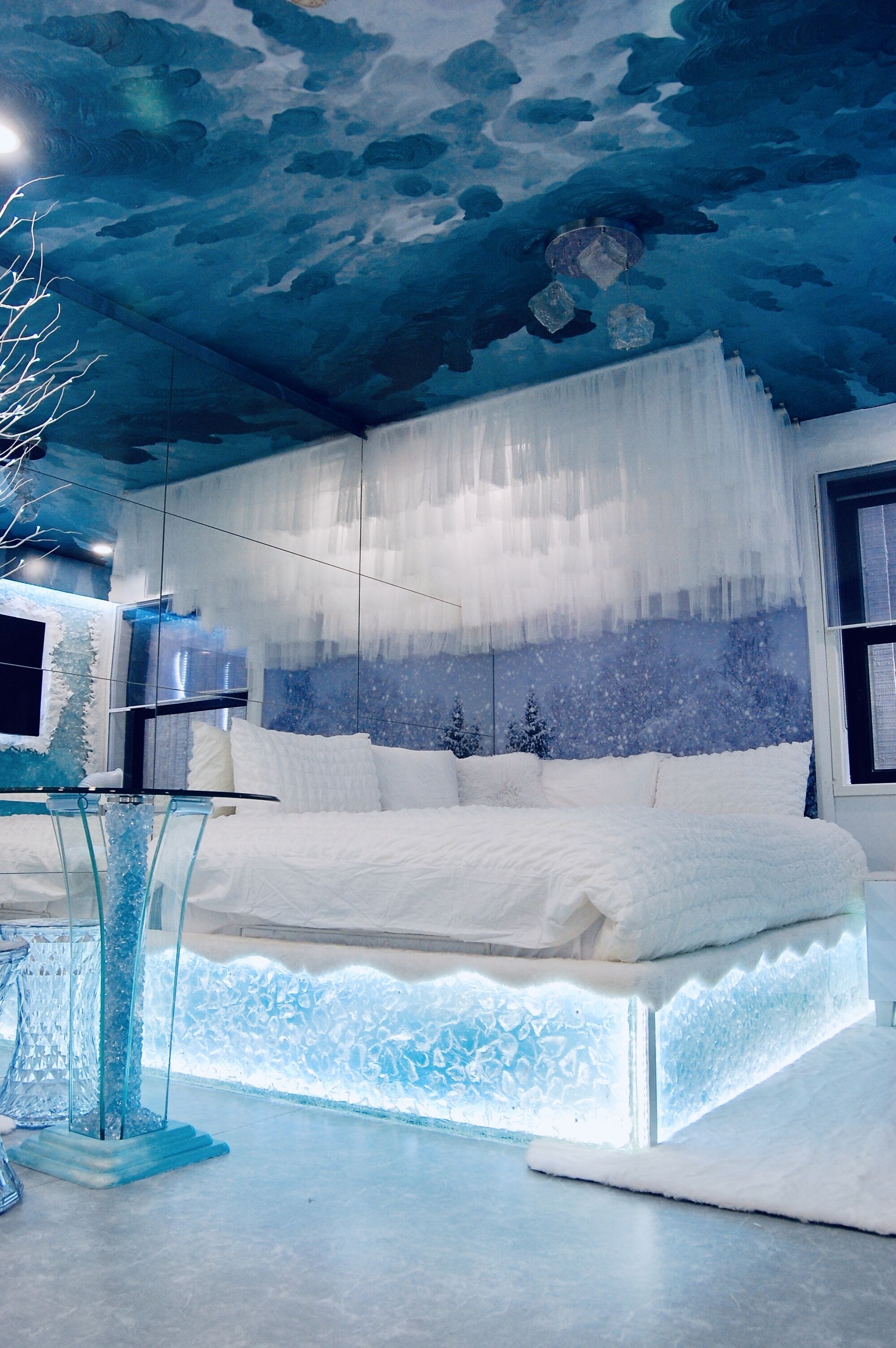 Een slaapkamer met een bed, een glazen tafel en een plafond met een wolkenmotief.