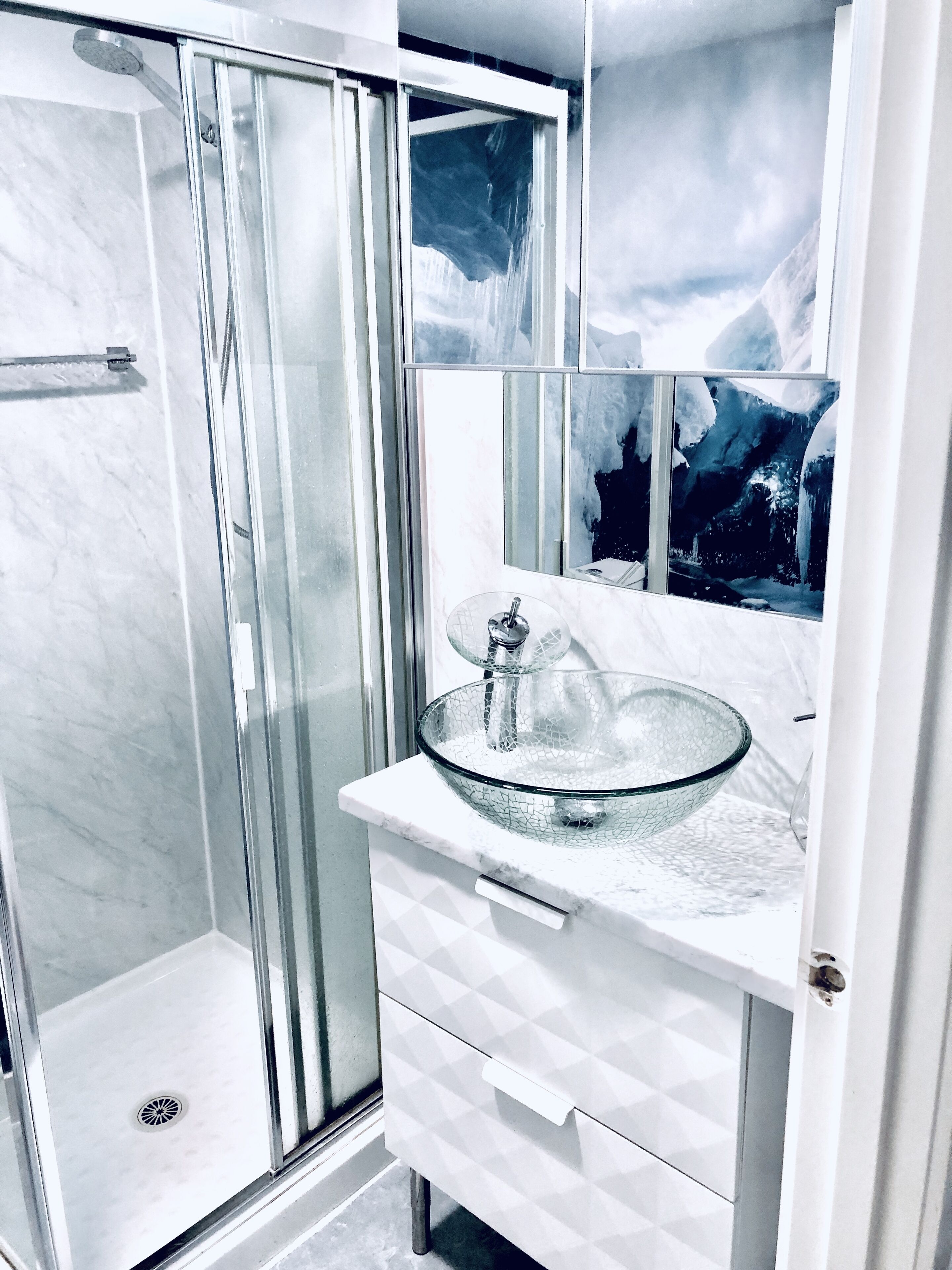 Une salle de bain dotée d’une douche en verre, d’un lavabo en marbre et d’un grand miroir qui reflète un paysage montagneux.