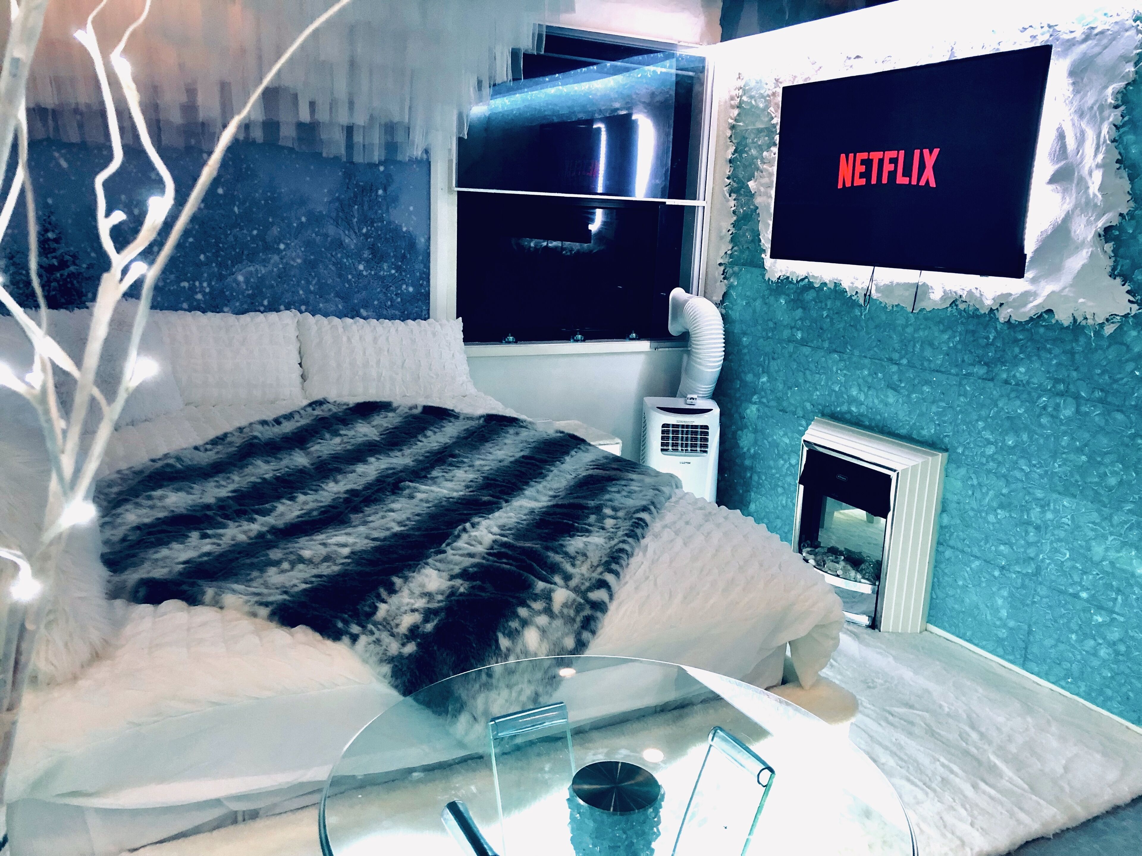 Une chambre avec un lit, une table en verre, un radiateur et un téléviseur fixé au mur qui affiche le logo de Netflix.