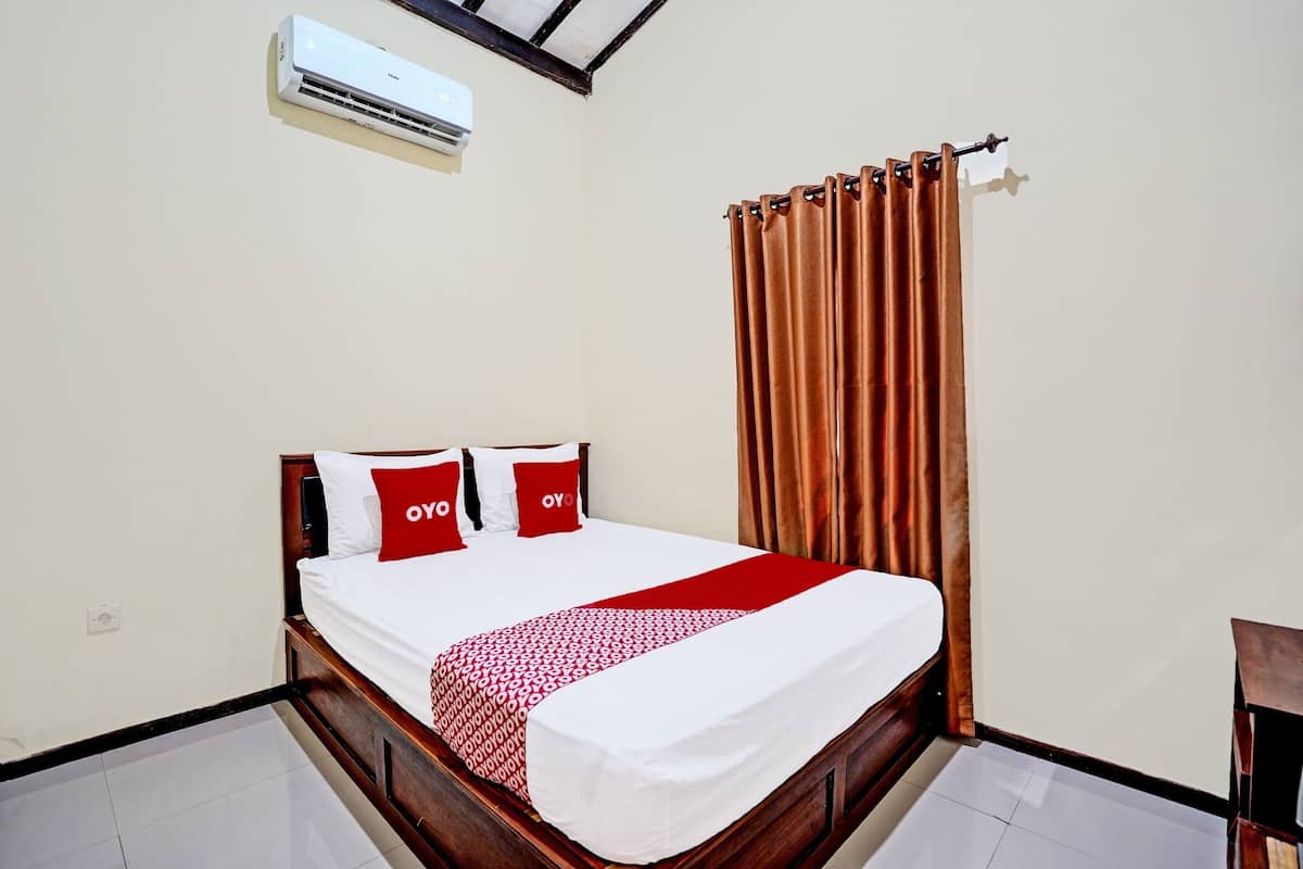 A neatly made bed with a white and red bedspread, two pillows with the word "OY" on them, and a brown curtain on the window.