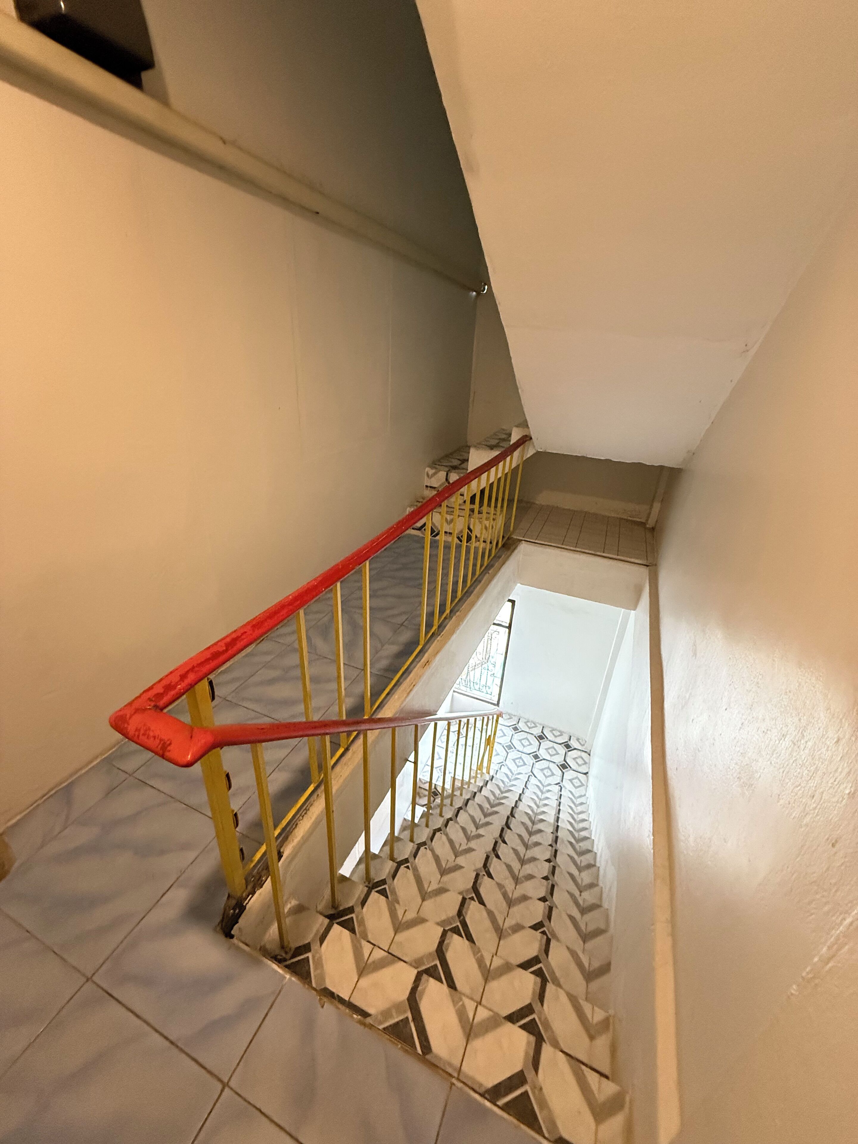 A staircase with a red handrail and patterned floor tiles.