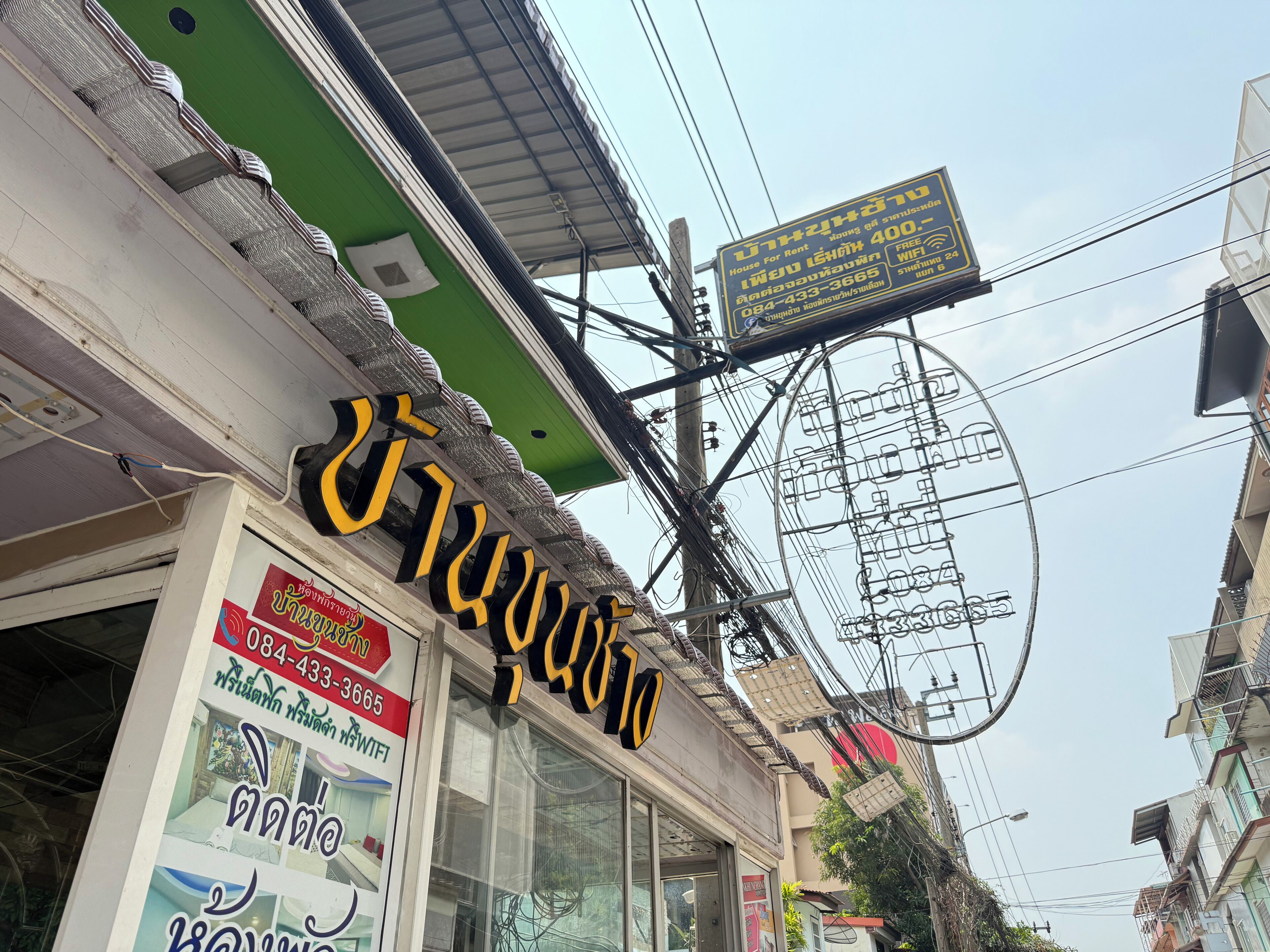 A building with a signboard advertising a house for rent and a contact number.