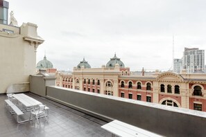 A rooftop terrace with a long table and benches, overlooking a historic building with domed structures. - Secret Garden - A Magical Themed Studio in the heart of Melbourne CBD (Melbourne,)