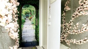 A hallway with a stone pathway leading to a garden, a door with a doormat, and a wall with a floral design. - Secret Garden - A Magical Themed Studio in the heart of Melbourne CBD (Melbourne,)