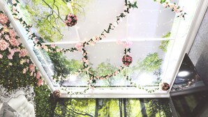 A room with a large skylight, decorated with pink flowers and greenery, and a view of trees outside. - Secret Garden - A Magical Themed Studio in the heart of Melbourne CBD (Melbourne,)