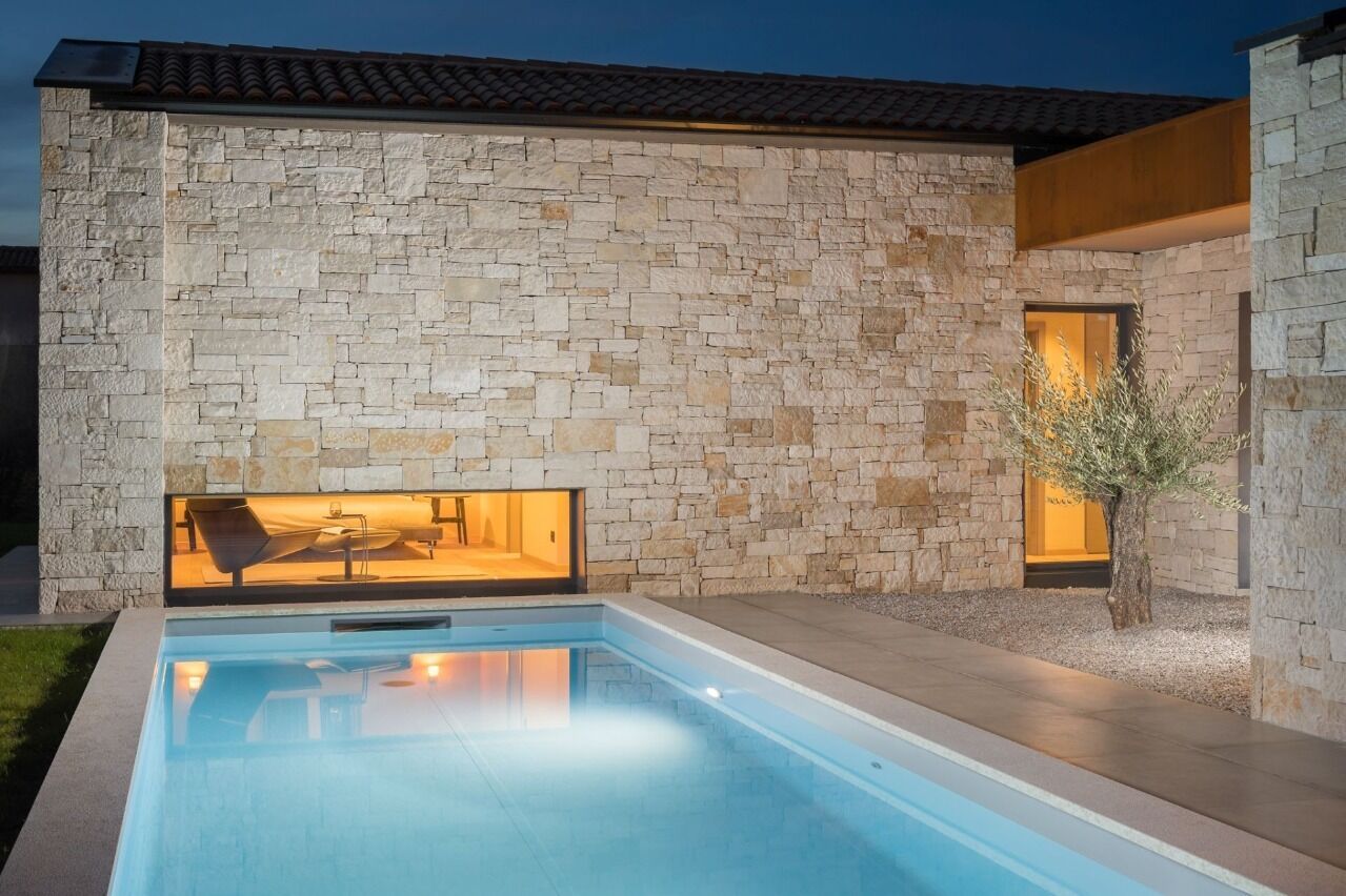 Un edificio moderno con fachada de piedra, piscina e interiores luminosos.