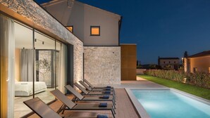 A modern poolside area with lounge chairs and a glass-enclosed bedroom.