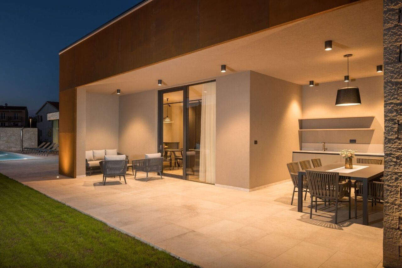 Ein moderner Außenbereich mit Terrasse, ausgestattet mit Esstisch und Stühlen, einer Couch und einer Glastür zu einem Innenraum.