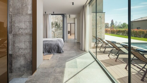 A modern hotel room with a large window, a view of the outdoor pool, and a stone wall.
