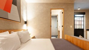 A hotel room with a large bed, a wooden headboard, a bedside table, and a nightstand. There is a mirror on the wall and a door leading to another room. - Beautiful apt w/ terrace @Parque Mexico | ChiCo (Ciudad de México)