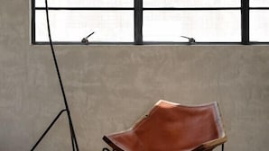 Ein Zimmer mit einem großen Fenster, einer schwarzen Stehlampe und einem braunen Ledersessel auf einem Teppich.