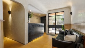 Ein Empfangsbereich im modernen Stil, mit einer Rezeption, einer Sitzecke inklusive Sofa und Sesseln sowie einer großen Glasdoor, die nach draußen führt.