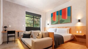 Quarto de hotel moderno com sofá, cama, escrivaninha e janela com vista para árvores.