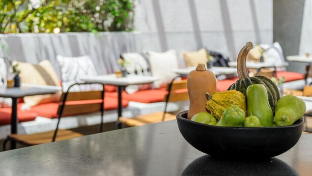 Un bol de légumes est posé sur une table dans un restaurant. Les sièges sont rembourrés de rouge et un mur blanc se trouve à l’arrière-plan.
