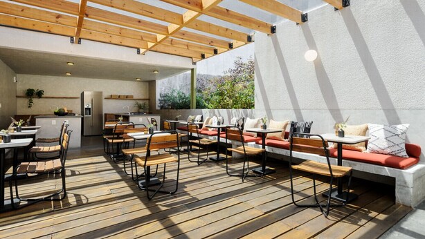 Un patio exterior con piso de madera, zonas de estar y una cocina.