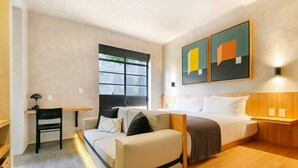 A compact hotel room with a bed, a sofa, a desk, and a window.
