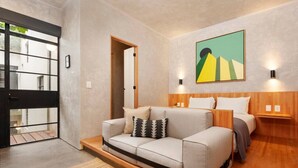 A modern living room with a sofa, a bed, and a wooden headboard. There is a painting on the wall and a door with a metal frame. - Design apt with Balcony @Parque Mexico | ChiCo (Ciudad de México)