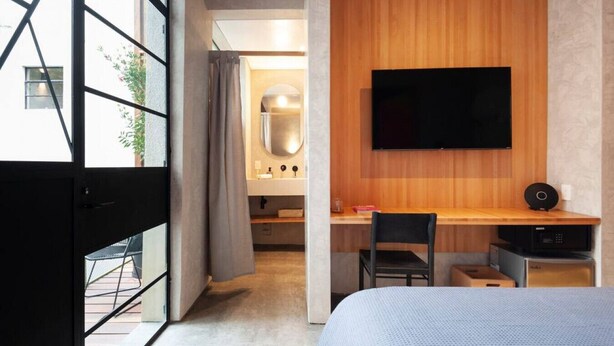A modern hotel room with a large bed, a desk with a chair, a TV mounted on the wall, and a bathroom visible through an open door. - Radiant studio with Balcony @Parque Mexico | ChiCo (Ciudad de México)