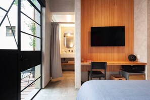 Habitació d'hotel moderna amb un llit gran, escriptori amb cadira, televisió penjada a la paret i un bany visible a través d'una porta oberta.