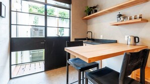 Une cuisine de taille réduite avec une table en bois, des chaises noires, une porte noire et une fenêtre donnant sur un paysage verdoyant.