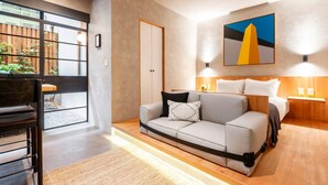 Une chambre d’hôtel moderne avec un canapé-lit, une table de chevet en bois, un tableau au mur et une vue sur l’extérieur grâce à une porte coulissante.