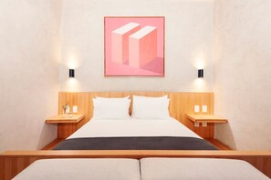 Une chambre d’hôtel moderne avec un grand lit, une tête de lit en bois, deux tables de chevet avec des lampes et une œuvre d’art abstraite encadrée au-dessus du lit.