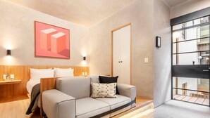 Een moderne hotelkamer met een bank, een bed, een nachtkastje, een wandlamp en een groot raam.