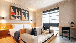 Ein modernes Hotelzimmer mit Bett, Sofa, Schreibtisch und einem großen Fenster.